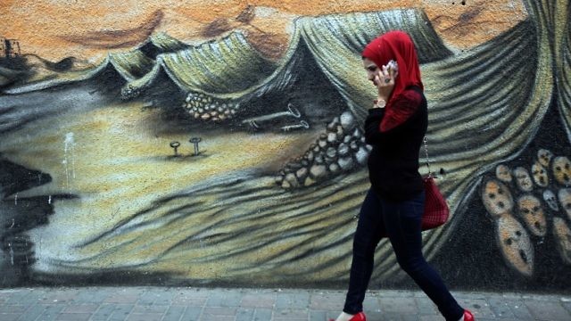 شابة فلسطينية في رام الله تمر بالقرب من رسم جرافيتي عن النكبة الفلسطينية (AFP)