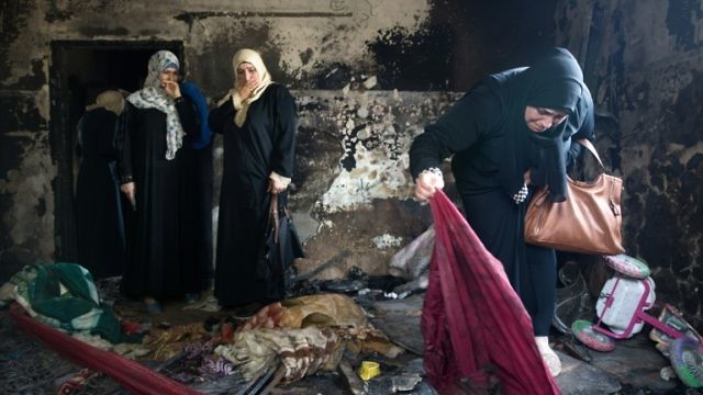 فلسطينيات يعاين الدمار الذي تسبب به الحريق في منزل الدوابشة في دوما (AFP)