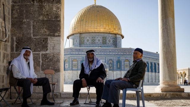 رجال فلسطينيون يجلسون في باحة الحرم القدسي الشريف وخلفهم قبة الصخرة (Sebi Berens/Flash90)