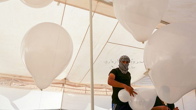 فلسطينيون يصنعون بالونات ستعلق على مواد قابلة للاشتعال ، خلال اشتباكات مع قوات الأمن الإسرائيلية على الحدود مع غزة (FLASH 90)